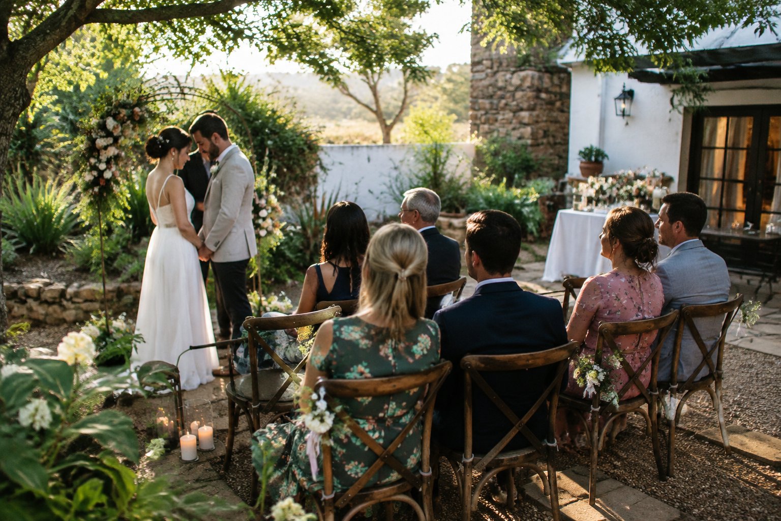 A couple shares a quiet moment at a small garden wedding with a few guests seated nearby.