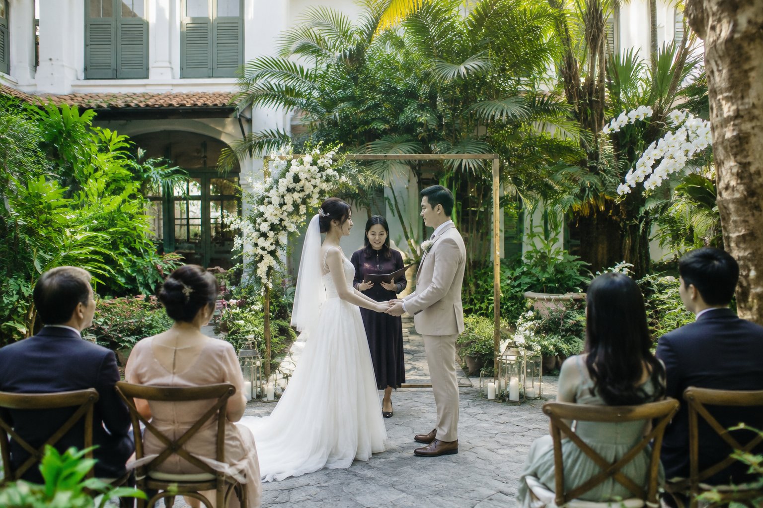 A couple exchange wedding vows in a garden courtyard as a small group of guests watches.