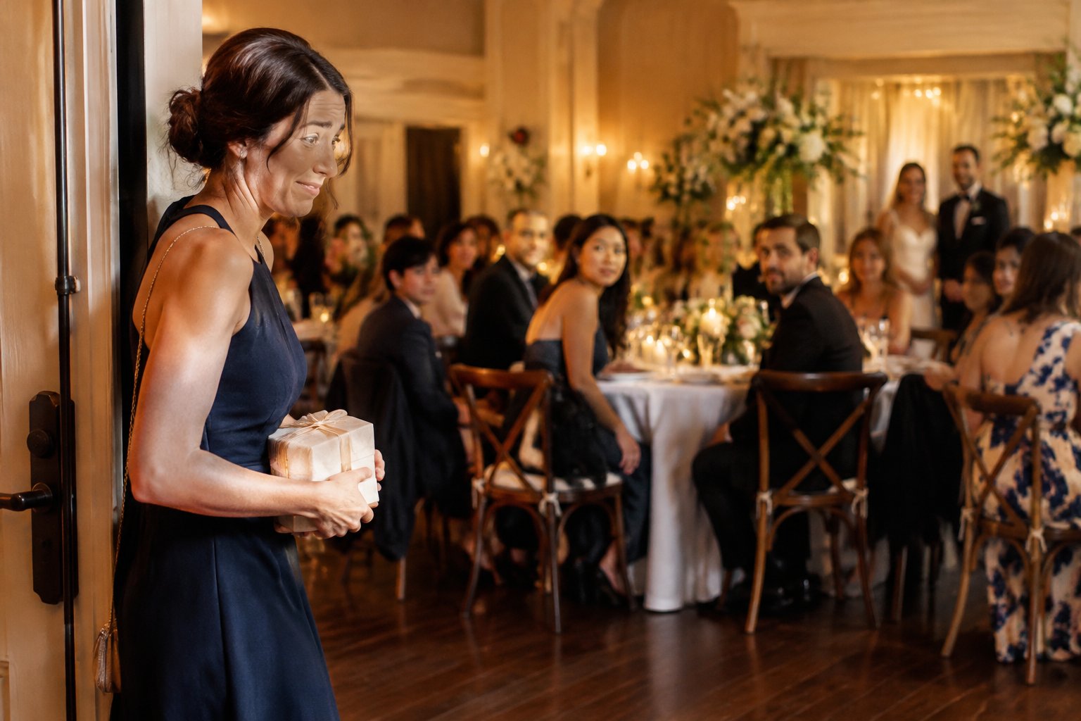 A wedding guest arrives at the reception as seated guests look toward the entrance.