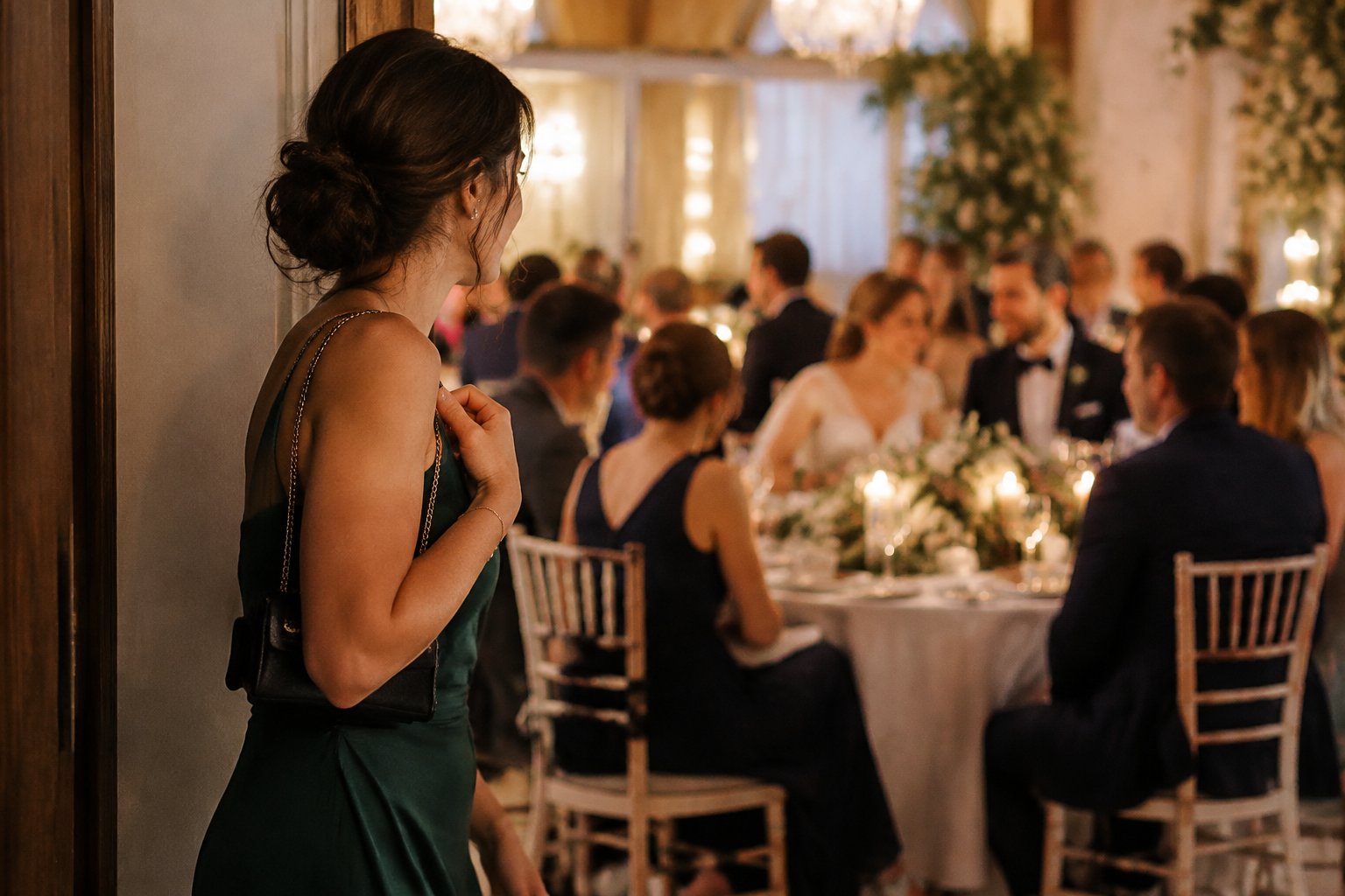 A formally dressed guest quietly arrives while a wedding reception is underway.