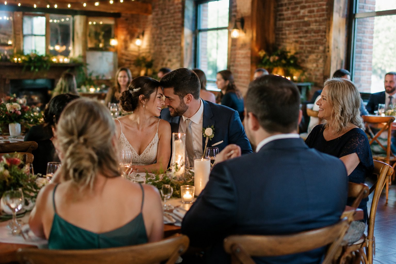 A couple celebrates with a small group of family and friends in a warmly lit wedding venue.