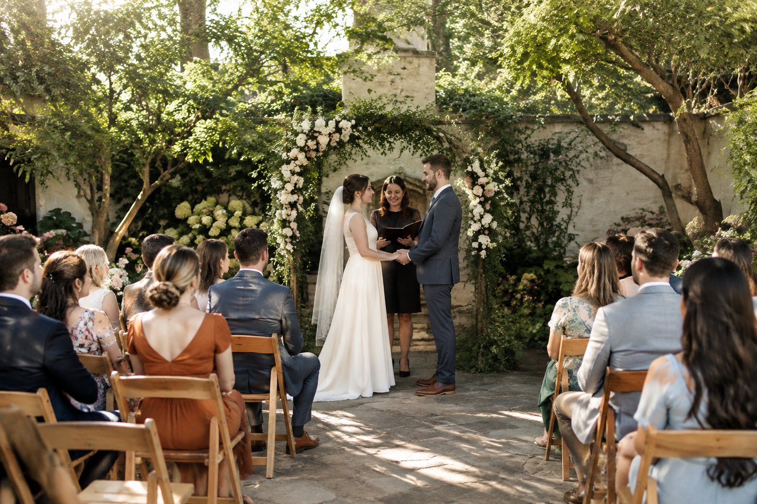 A couple exchanges vows before a small group of guests in a garden.