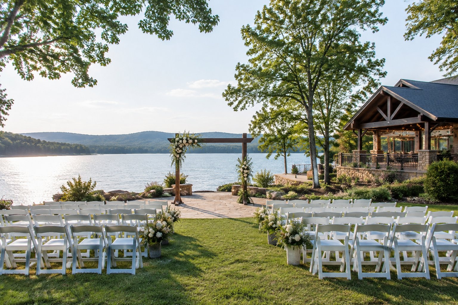 A wedding ceremony setup beside a lake, with rows of chairs, a floral arch, and a pavilion nearby.